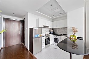 A modern kitchen with white cabinets, stainless steel appliances, and a black countertop. - Silkhaus Studio in Silicon Oasis City View (Dubai)