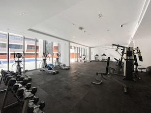 A spacious gym with treadmills, elliptical machines, and weightlifting equipment. Large windows offer views of the outside. - Silkhaus Studio in Silicon Oasis City View (Dubai)