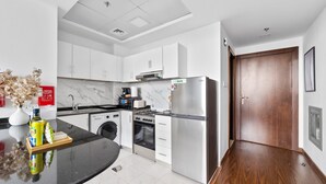 A modern kitchen with white cabinets, a stainless steel refrigerator, and a built-in oven. - Silkhaus Cozy Studio Balcony Binghatti Pearl (Dubai)