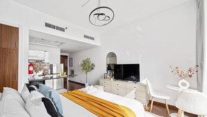 A modern hotel room with a large bed, a desk, a television, and a kitchenette in the background. - Silkhaus Cozy Studio Balcony Binghatti Pearl (Dubai)