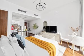 Ein modernes Hotelzimmer mit einem großen Bett, einem Schreibtisch, einem Fernseher und einer kleinen Küche im Hintergrund.