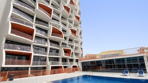 A modern building with multiple balconies, a swimming pool, and a covered area with seating. - Silkhaus Cozy Studio Balcony Binghatti Pearl (Dubai)