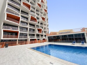 Ein modernes Gebäude mit mehreren Balkonen, einem Schwimmbad und einem überdachten Bereich mit Sitzgelegenheiten.