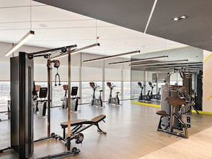 Ein Fitnessstudio mit unterschiedlichen Trainingsgeräten, großen Fenstern und Blick auf die Stadt.