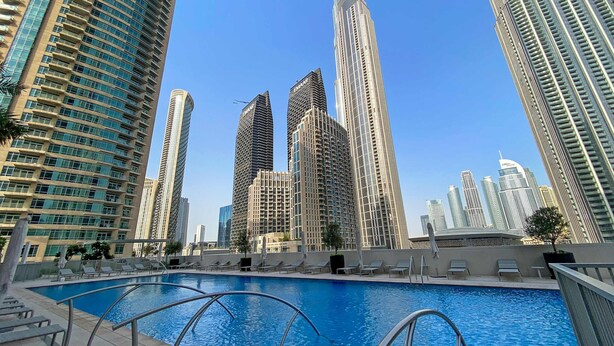 Ein Schwimmbecken mit Liegestühlen und einer Skyline hoher Gebäude im Hintergrund.