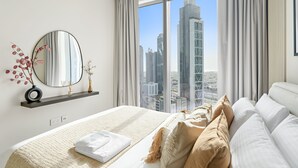 Ein modernes Hotelzimmer mit einem großen Bett, einem runden Spiegel, Blick auf Wolkenkratzer der Stadt und einem Vorhangfenster.