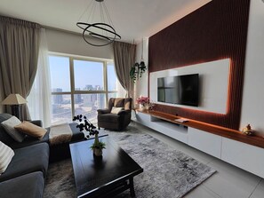 A modern living room with a large TV, comfortable seating, a coffee table, and a view of the city. - Silkhaus Cozy 1BR With Balcony Pool Gym on Reem Island (Abu Dhabi)