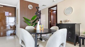 A modern dining area with a round table, four chairs, a dark wooden cabinet, and a potted plant. - Silkhaus Cozy 1BR With Balcony Pool Gym on Reem Island (Abu Dhabi)