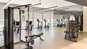 A modern gym with various exercise equipment, large windows, and a city view. - Silkhaus New High Floor Studio Aykon City (Dubai)