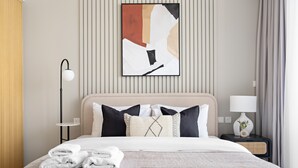 A hotel room with a bed, pillows, a bedside table with a lamp, and a wall art piece. - Silkhaus New High Floor Studio Aykon City (Dubai)