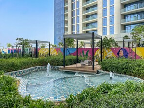 A pool area with two fountains, surrounded by greenery and a colorful mural. - Silkhaus New High Floor Studio Aykon City (Dubai)