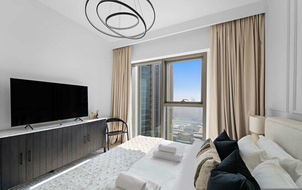Ein modernes Hotelzimmer mit einem großen Bett, einem Flachbildfernseher, einem Schreibtisch mit Stuhl und einem großen Fenster mit Blick auf die Stadt.