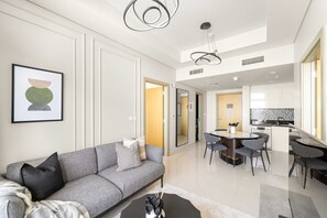 A modern living room with a grey sofa, a coffee table, and a dining area with a round table and chairs. - Silkhaus Elite 2bdr Near Safa Park Aykon City (Dubai)