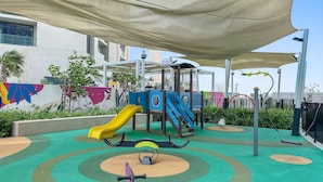 A playground with a slide, swings, and a climbing structure. - Silkhaus Elite 2bdr Near Safa Park Aykon City (Dubai)