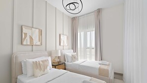 A hotel room with two beds, a nightstand, a lamp, and artwork on the walls. - Silkhaus Cozy 2 BR Full Amenities (Dubai)