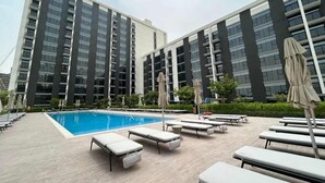 A modern hotel with a swimming pool, sun loungers, and a well-maintained garden area. - Silkhaus Cozy 2 BR Full Amenities (Dubai)
