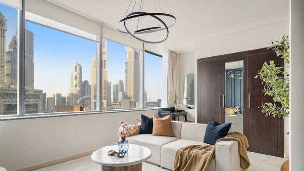 A modern living room with a large window, a round coffee table, a sofa, and a view of a city skyline. - Silkhaus Cozy Studio Sky Gardens Heart of Difc (Dubai)