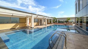 A modern outdoor swimming pool with clear blue tiles, surrounded by a tiled deck and a building with large windows. - Silkhaus Cozy Studio Sky Gardens Heart of Difc (Dubai)