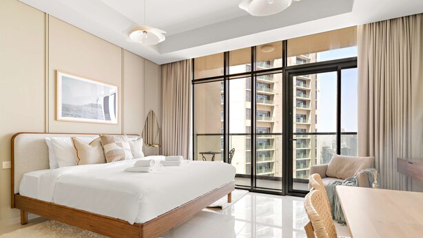 Habitación de hotel moderna con una cama grande, zona de comedor y vistas a edificios altos.
