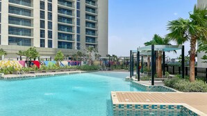 Una piscina con borde de baldosas, rodeada de palmeras y un edificio con balcones.