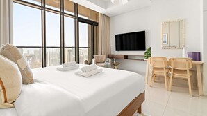 Habitación de hotel con una cama grande, televisor, escritorio con sillas y vista a la ciudad.