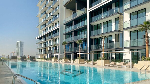 Ett modernt hotell med en swimmingpool, flera balkonger och utsikt över en hög byggnad i bakgrunden.
