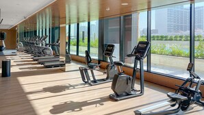 Ett gym med träningsutrustning, stora fönster och utsikt över byggnader.