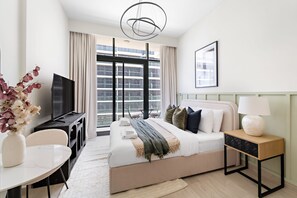 A modern hotel room with a large bed, a TV, a desk, and a view of the city through large windows. - Silkhaus Chic Studio Skyline View MBR City (Dubai)