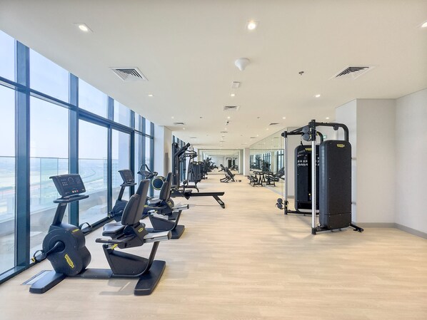 Ein modernes Fitnessstudio mit Laufbändern, Krafttrainingsgeräten und großen Fenstern mit Blick auf die Stadt.