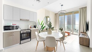 Een moderne keuken met een fornuis, magnetron en spoelbak, een eethoek met een ronde tafel en stoelen, en een groot raam met uitzicht op de stad.