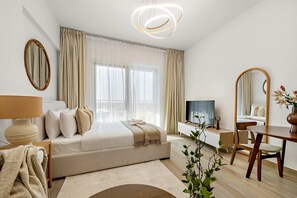 Et moderne hotelværelse med en stor seng, et skrivebord, en stol, et fjernsyn og et spejl.