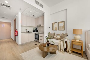 A modern living room with a sofa, coffee table, and a small side table. There is a kitchen area with cabinets and appliances visible through an open doorway. - Silkhaus Chic Studio Stay Near Ferrari World (Abu Dhabi)