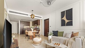 A modern living room with a flat-screen TV, a dining area with a round table and chairs, a sofa with cushions, and a coffee table with snacks. - Silkhaus Comfy 1bdr Sky Gardens in Difc NEW (Dubai)