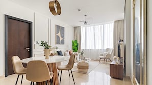 A modern living room with a round dining table, beige chairs, a coffee table, and a large window with curtains. - Silkhaus Comfy 1bdr Sky Gardens in Difc NEW (Dubai)