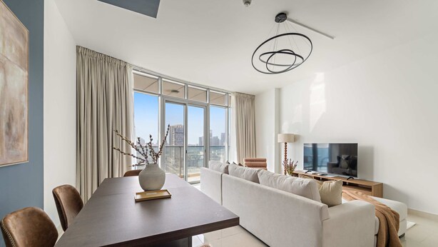 A modern living room with a dining area, large windows, a sofa, and a television. - Silkhaus New 2bdr in Julphar Near Adgm (Abu Dhabi)