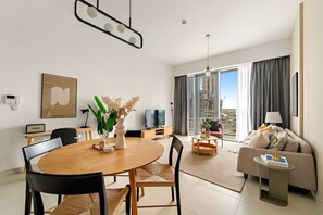 A modern living room with a dining area, a sofa, a TV, and a large window with curtains. - Silkhaus Elite 3BR Near Dubai Watercanal in Al Wasl (Dubai)