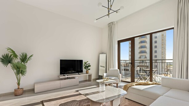 A modern living room with a sofa, a coffee table, a TV, and a balcony with outdoor furniture. - Silkhaus Premier 1BR Yas Golf Collection (Abu Dhabi)