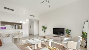 A modern living room with a sofa, coffee table, and armchair, a dining area with a table and chairs, a kitchen with a refrigerator, and a TV. - Silkhaus Premier 1BR Yas Golf Collection (Abu Dhabi)
