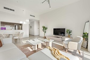 A modern living room with a sofa, coffee table, and armchair, a dining area with a table and chairs, a kitchen with a refrigerator, and a TV. - Silkhaus Premier 1BR Yas Golf Collection (Abu Dhabi)