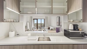 A modern kitchen with a built-in sink, a coffee machine, and a view of the city through large windows. - Silkhaus Premier 1BR Yas Golf Collection (Abu Dhabi)