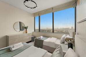 A modern hotel room with two beds, a large window with a city view, a round mirror, and a decorative ceiling light. - Silkhaus Expansive 2bdr in Sky Gardens Difc (Dubai)
