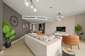A modern living room with a sectional sofa, a brown armchair, a round coffee table, and a TV. - Silkhaus Expansive 2bdr in Sky Gardens Difc (Dubai)