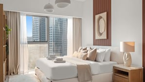 Een moderne slaapkamer met een groot bed, een nachtkastje, een lamp en uitzicht op een stadslandschap door een groot raam.