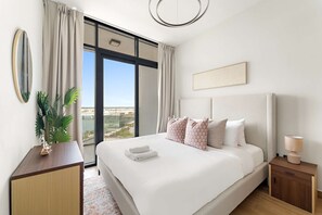 Une chambre d’hôtel moderne avec un grand lit, une table de chevet avec une lampe, une vue sur la ville par une grande fenêtre et une plante en pot sur une commode en bois.