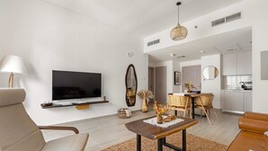 A modern living room with a flat-screen TV, a wooden coffee table, and a sofa. There is a dining area with a table and chairs, and a kitchen in the background. - Silkhaus Serene 1bdr Retreat in Yas Island (Abu Dhabi)