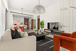 A modern living room with a sofa, coffee table, and orange armchair. A television and black cabinet are in the background. - Silkhaus Elite 1bdr Canal Front Tower Al Wasl (Dubai)