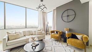 Ein modernes Wohnzimmer mit Sofa, Sessel und Couchtisch, großen Fenstern mit Blick auf die Stadt und einer außergewöhnlichen Wanduhr.