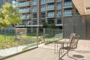 A modern outdoor seating area with a view of a multi-story building, a glass railing, and a tree. - Silkhaus Brand New 2bdr Myrtle in City Walk (Dubai)