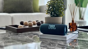 Een JBL speaker op een glazen tafel, met een boek, een plant en een diffuser.