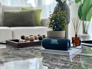 A JBL speaker on a glass table with a book, a plant, and a diffuser. - Silkhaus Brand New 2bdr Myrtle in City Walk (Dubai)